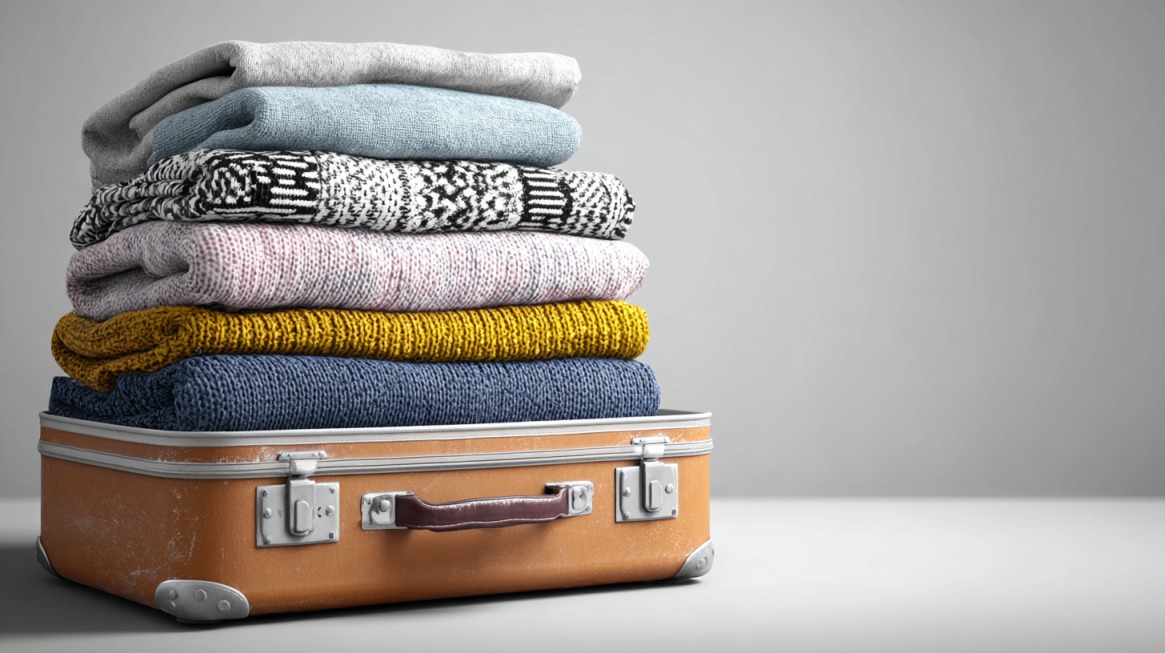 A small suitcase with a stack of folded sweaters piled high on top, overflowing beyond its capacity
