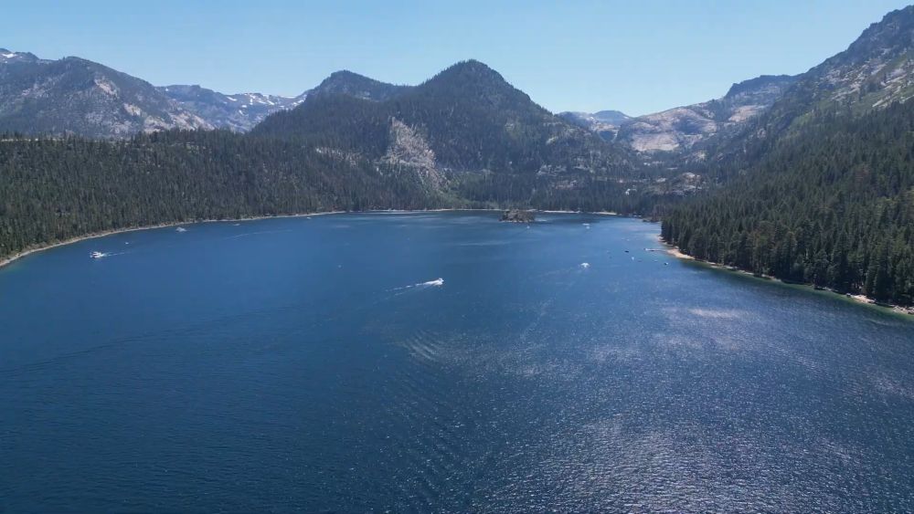 Aerial view of Lake Tahoe surrounded by forested mountains under clear blue skies