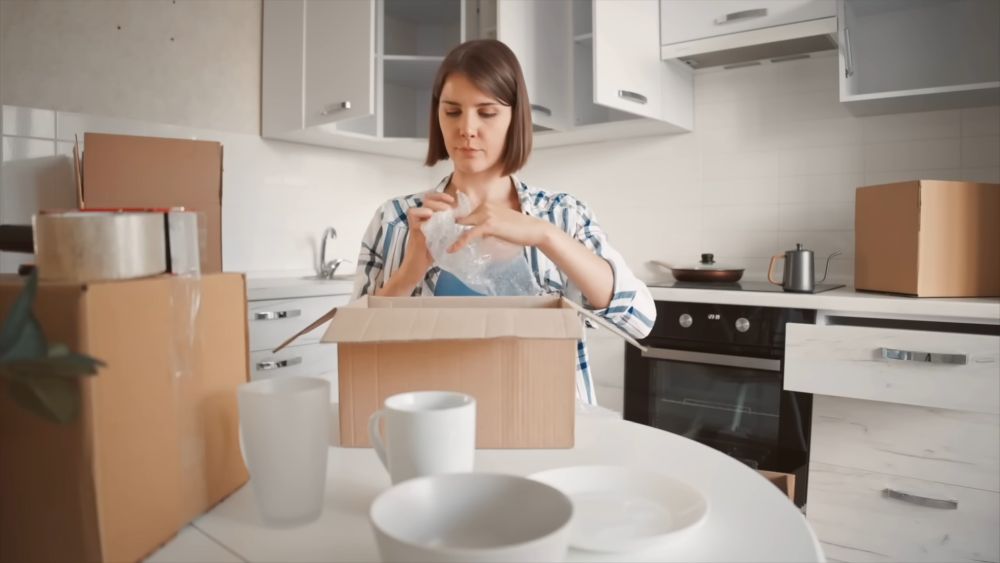 Woman packing kitchen items into moving box before relocating